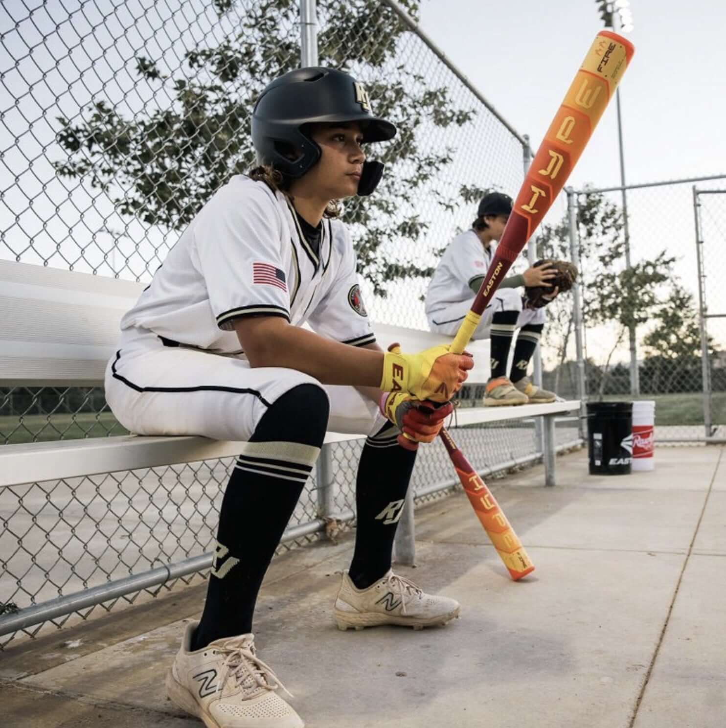 Baseball player in uniform sitting on bench holding a bat, preparing for the game on a sunny day