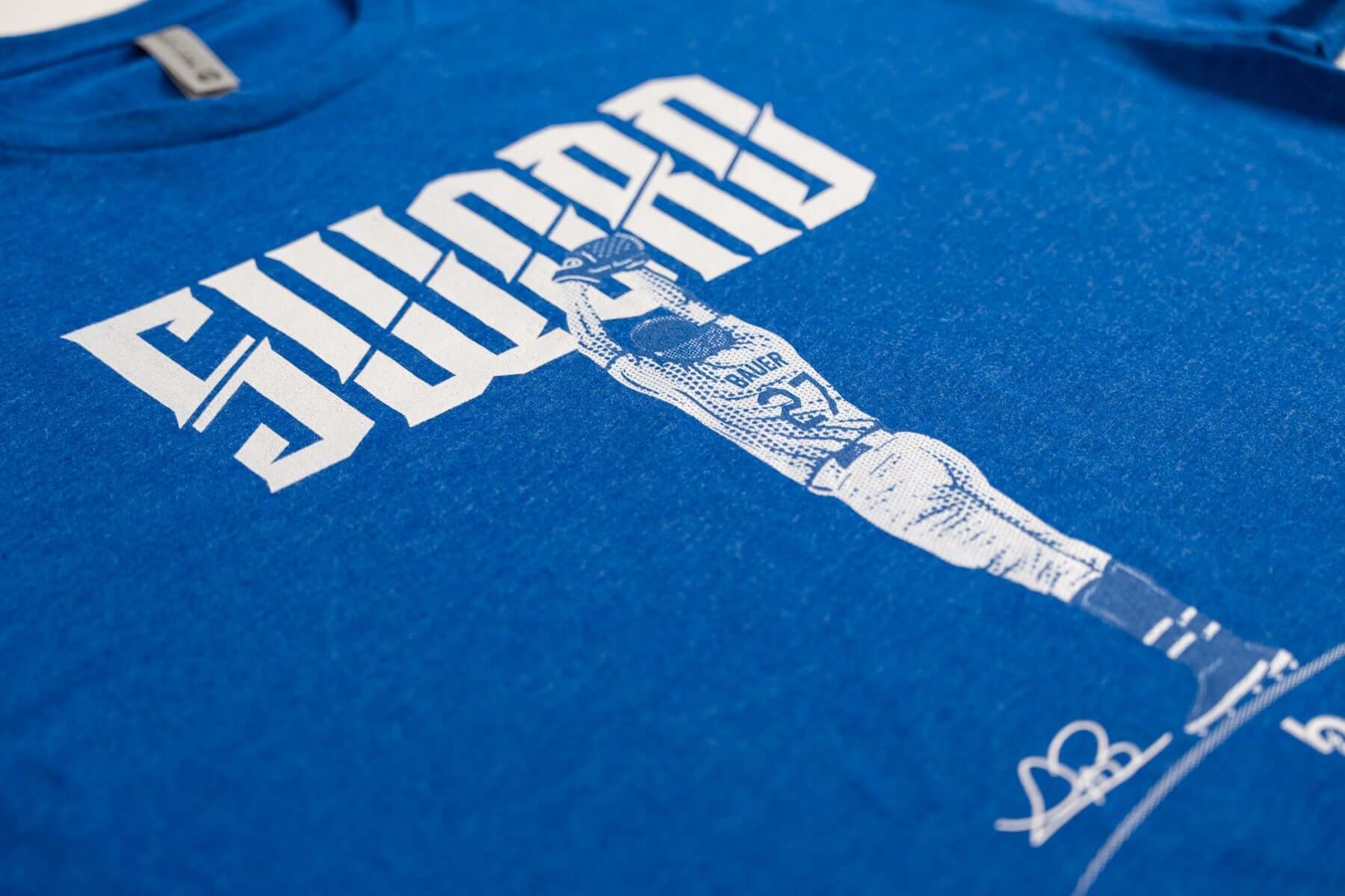 Bauer Outage Sword Tee featuring bold "SWORD" text and a graphic design of a player in action on a blue shirt.