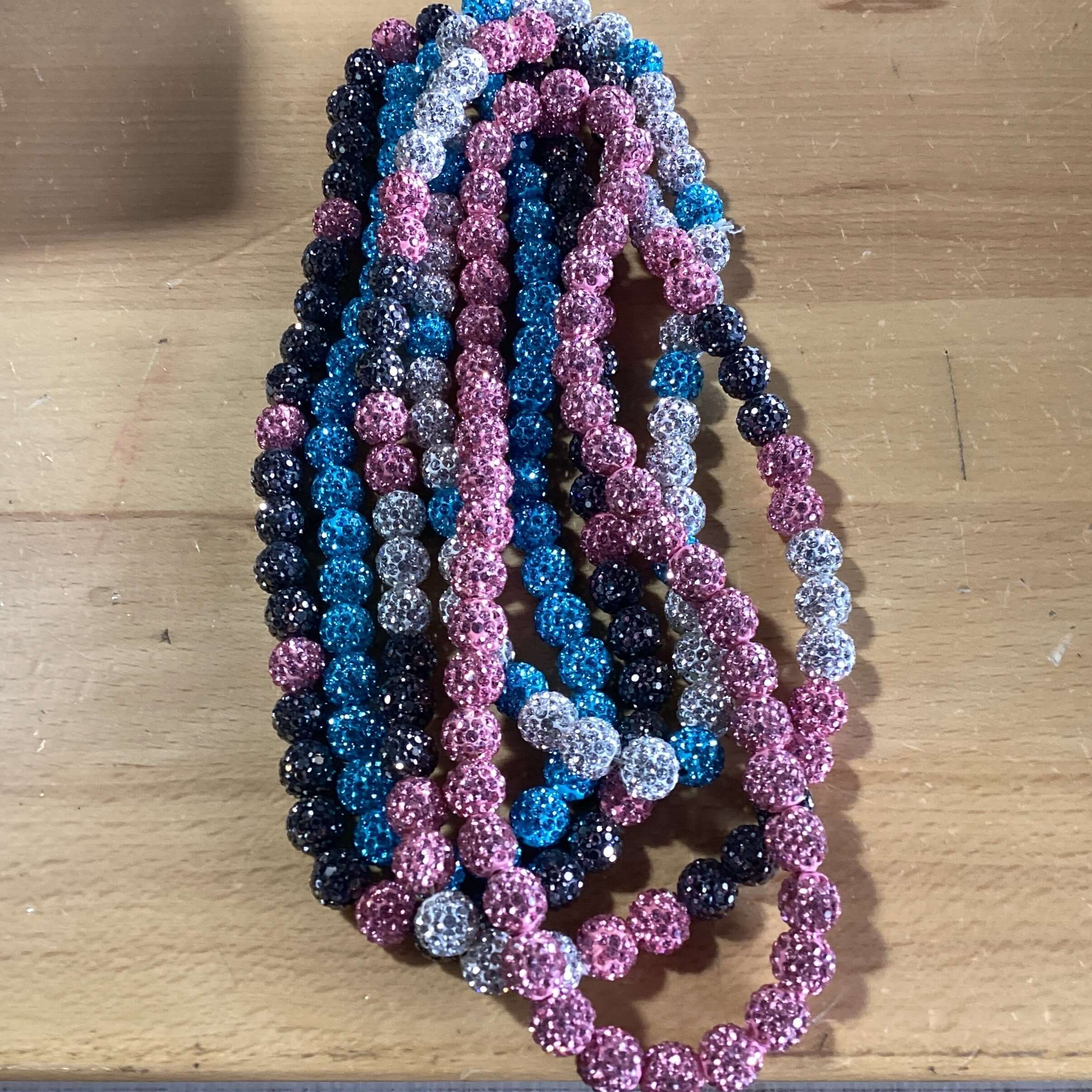 Colorful beaded necklaces in shades of pink, blue, gray, and black arranged on a wooden surface.